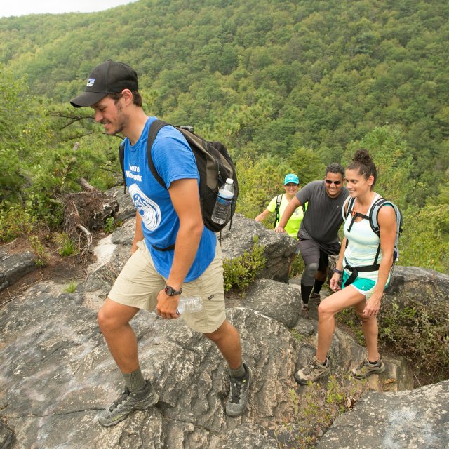Several hikers climbing a rocky mountain trail with wide views of the surrounding landscape.