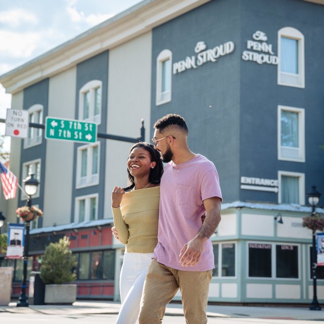 A couple walks arm in arm down a downtown street on a summer day.
