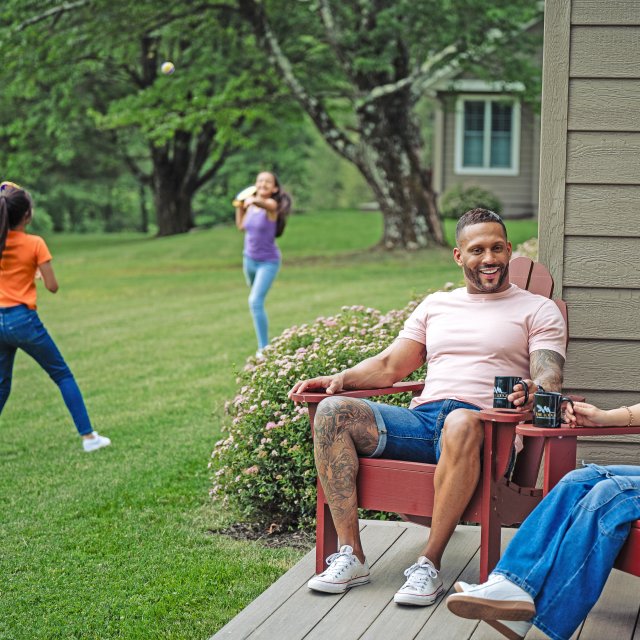 Parents relax in deck chairs while their daughters play outside nearby.