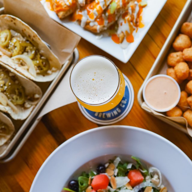 A table featuring appetizers alongside and a beer in the center.
