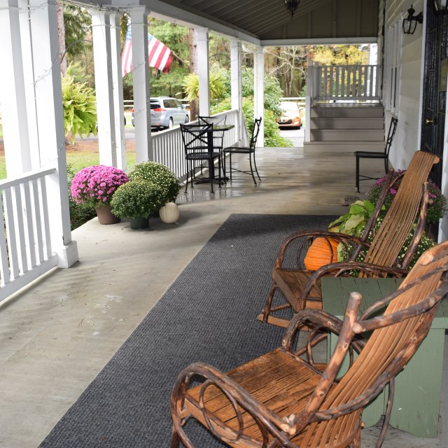 An outdoor porch at a lodge with rocking chairs and mums.