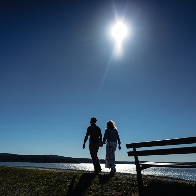 A couple holding hands while walking along a lakeside path.