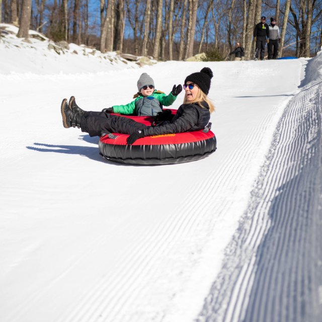 Mother and daughter snow tubing down a hill showing excitement