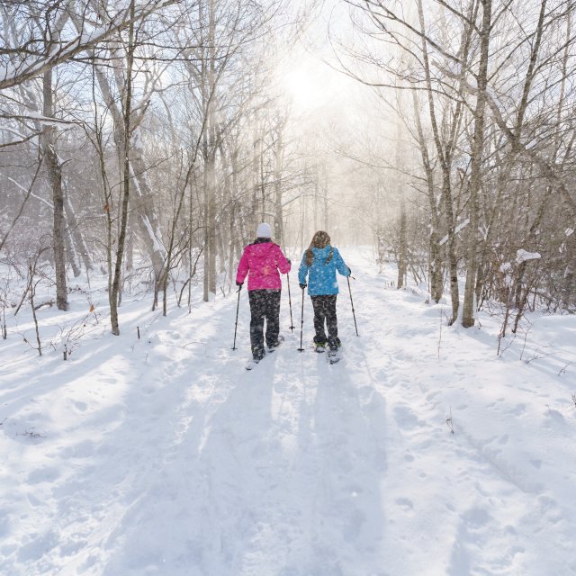 Two women snowshoeing on a trail while it is snowing