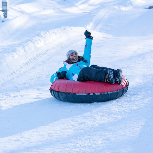 Women snow tubing down a hill showing excitement