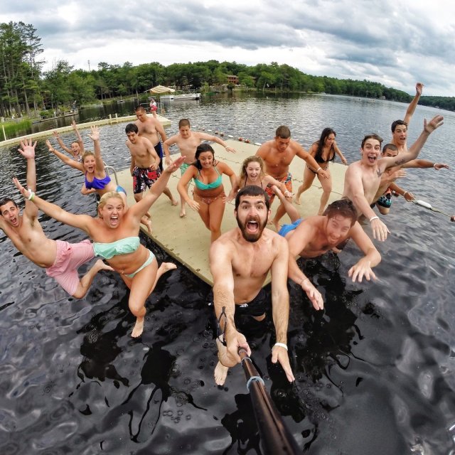 A group of friends jumping off a dock while taking a selfie