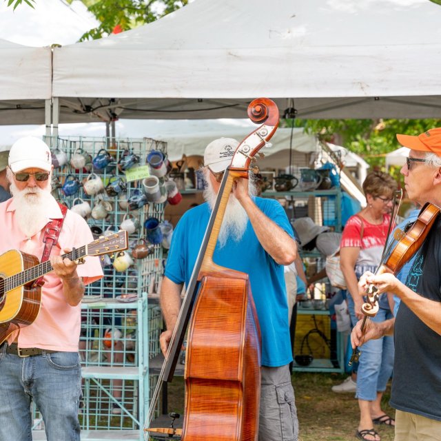 Three musicians playing instruments at an outdoor fair.