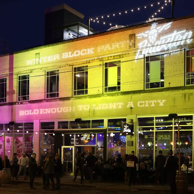 The building Braxton Brewing is located in, lit up with pink and yellow lights with the words Bold Enough to Light a City