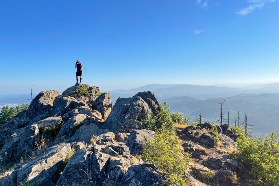 a man stands on top of a rocky summit with the valley down below.