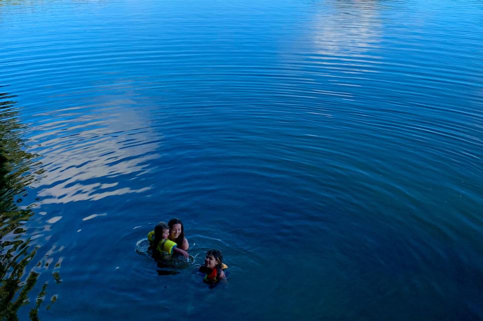 A woman and two young girls swim together in the deep blue waters at Dorena Lake which is surrounded by mountains.