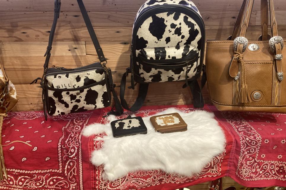 Cow print purses are displayed against a wood wall and red bandana draped shelf.