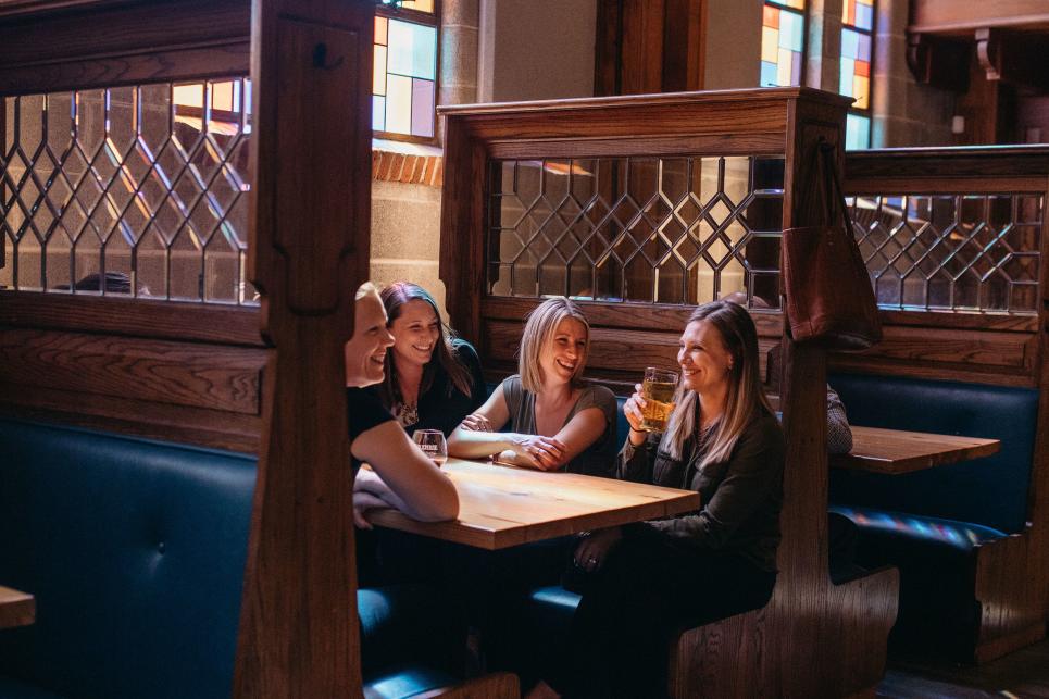 Women sit in a booth with stained glass behind them at PublicHouse.