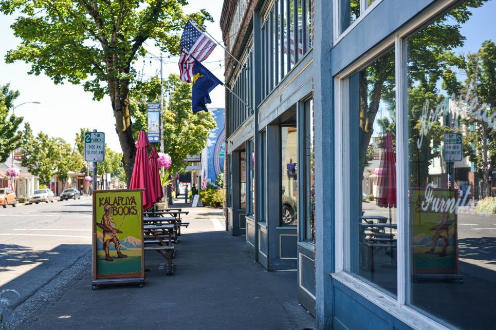 A storefront with American and Oregon flags and sandwich board for Kalapuya Books on the sidewalk.
