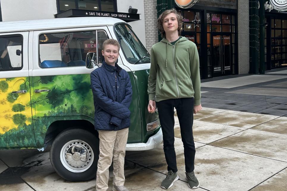 Two teens stand in front of a tie-dye painted green and yellow VW bus parked in the Market Alley plaza in front of The Gordon Hotel.