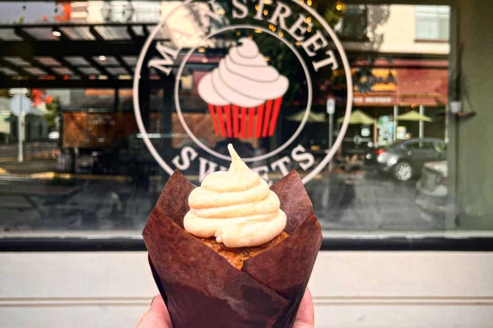 a hand holds a cupcake in front of a window with the main street sweets logo.