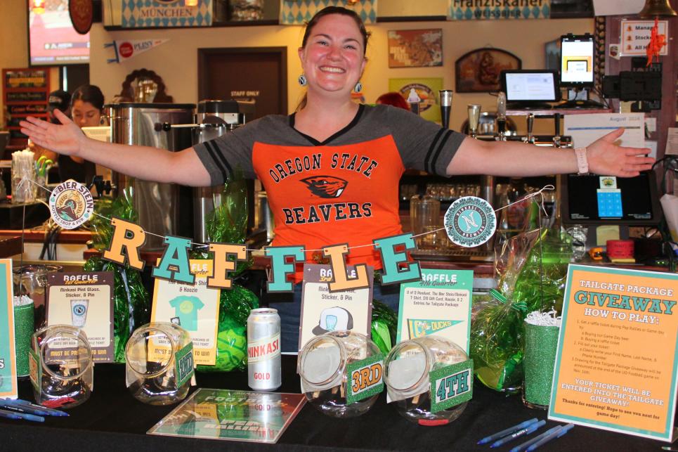 A person in an OSU Beaver shirt shows off the Duck green and yellow raffle table.