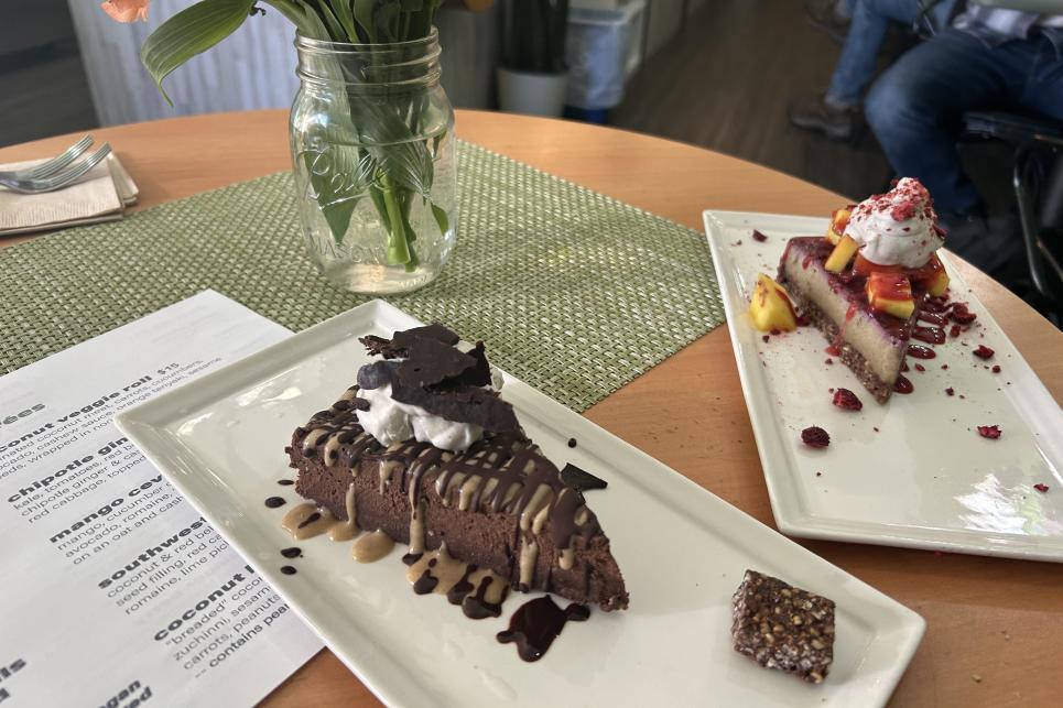 Two slices of pie, decked out with whipped cream and sauces, sit on white rectangle plates.