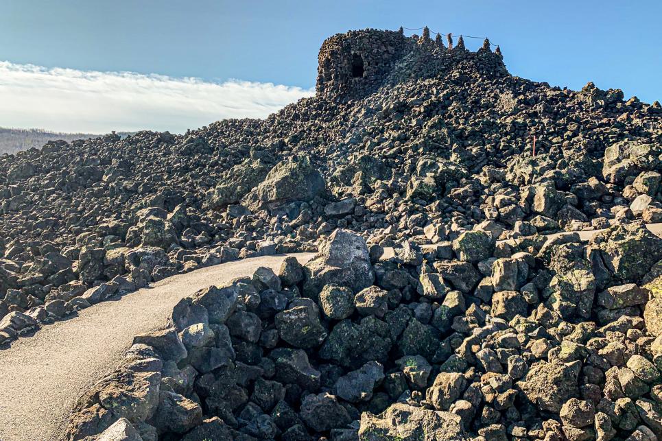 A paved path winds through a lava field upwards toward a rock fort.