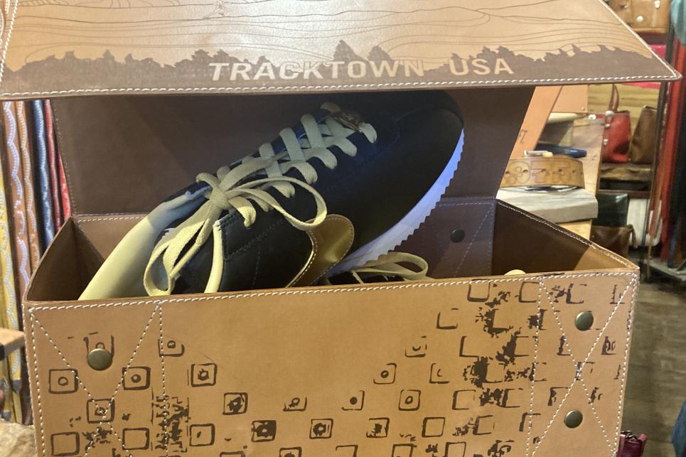 A leather shoe box with TrackTown USA embossed on it opens with special Nike shoes, black with yellow laces and a gold leather Nike swoosh.