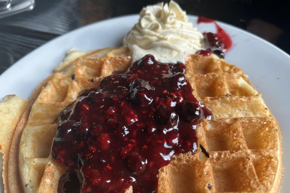 A close-up of a full round waffle topped with red berry compote and whipped cream.