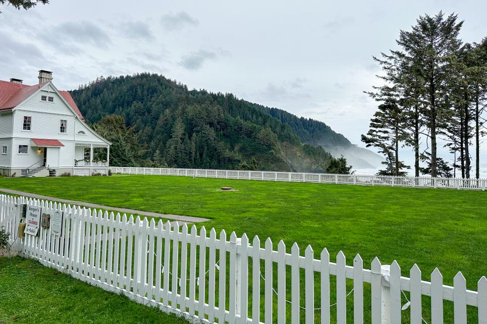 A grassy lawn in front of a victorian style white house sits on a coastal cliff with ocean in the background.