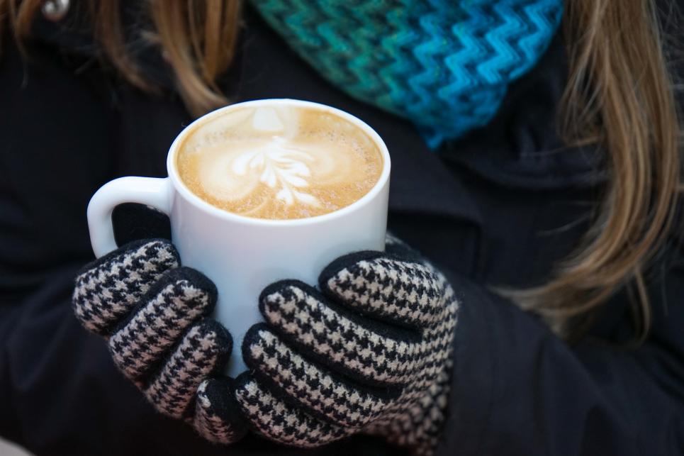 gloved hands hold a mug of coffee with latte art.