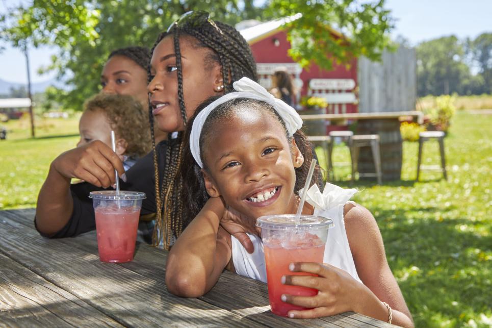 A girl at a picnic table smiles with her pink lemonade.