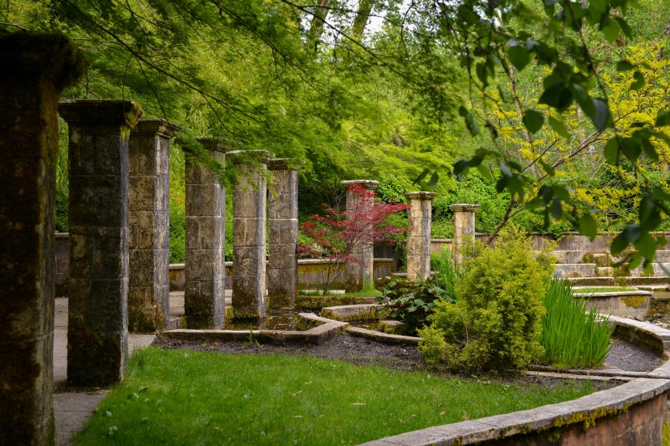 The Secret Garden at Belknap Hot Springs has stone pillars and stone lined pools of water. The garden is green with grass, landscaping and trees.