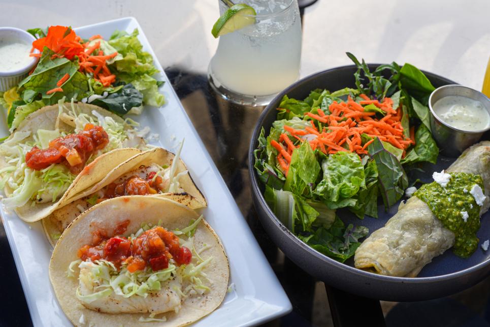 Fish tacos and seafood burrito with green sauce and a bright side salad