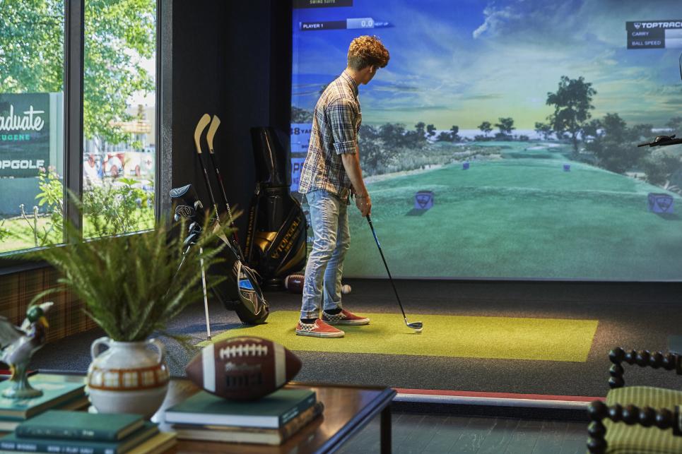 A person stands in front of a virtual driving range with his golf club.