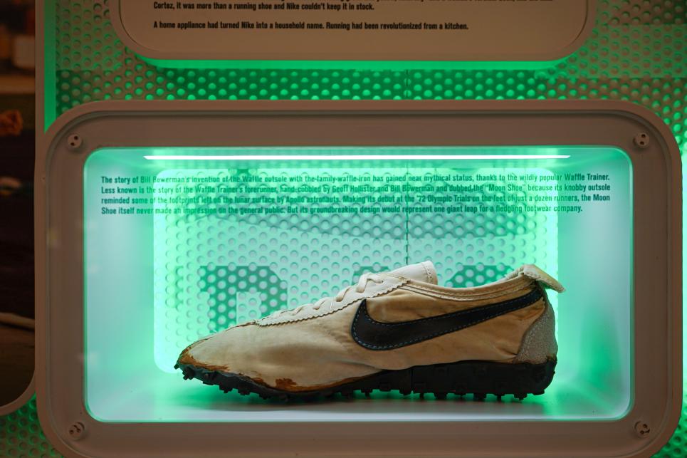 An early Nike shoe sits in a display case with green lights behind it.