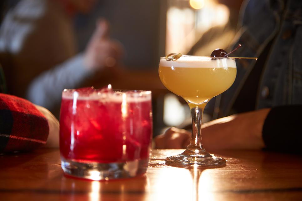 A pink drink in a short glass and a yellow cocktail in a coupe cocktail glass.