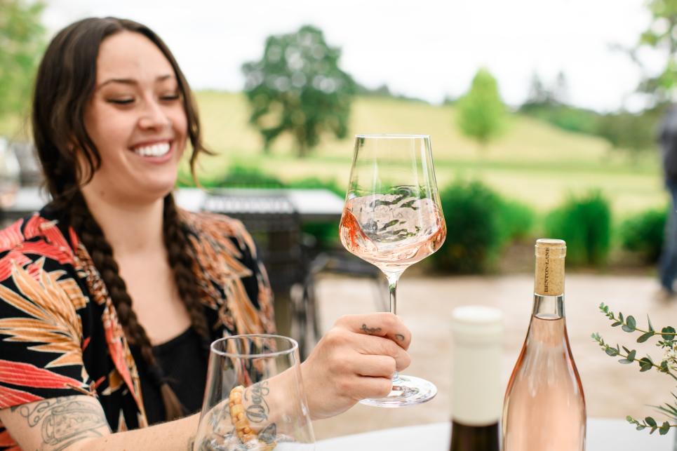 A woman smiles while swirling a glass of blush wine.
