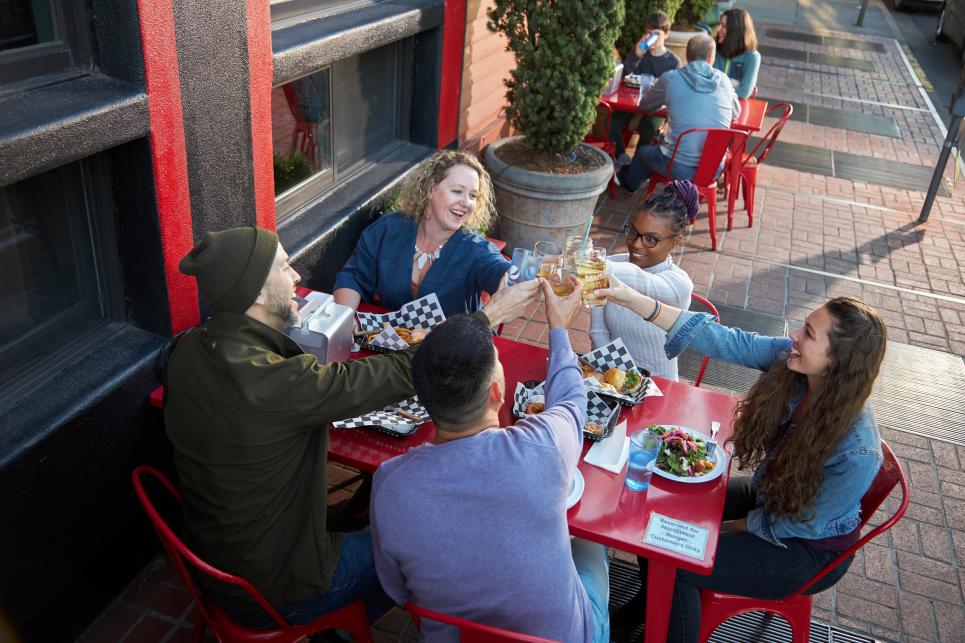 Five friends cheers at a red outdoor dining table.