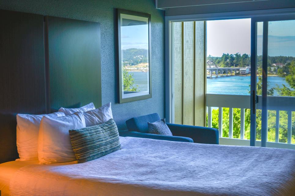 A hotel room bed with a balcony view of the Siuslaw Bay.