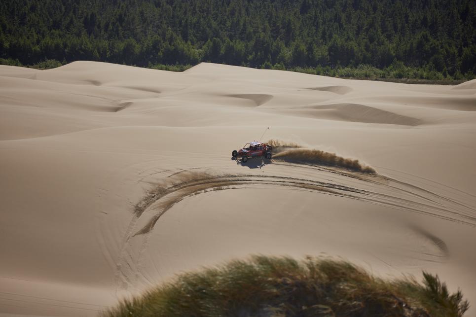 A dune buggy speeds over the Oregon dunes and sand flies up behind it.