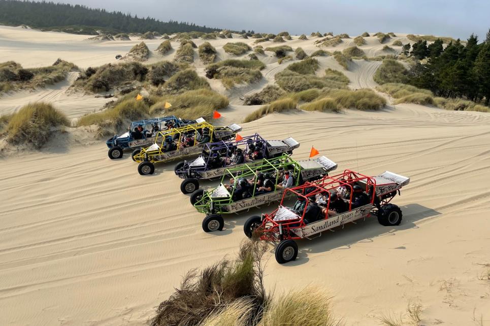 Five sandrails in rainbow colors line up on the sand dunes.