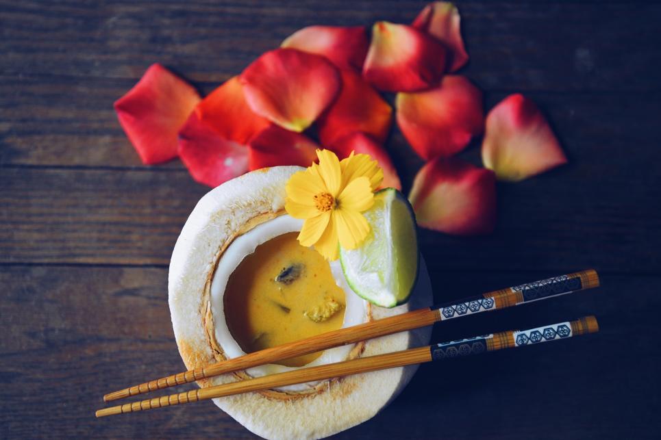 Tom Kha soup in a young coconut with lime, flowers and chopsticks in the scene.