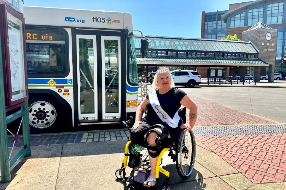 Melinda in her tiara and Ms. Wheelchair sash in front of an LTD bus at the Downtown Eugene LTD Station.