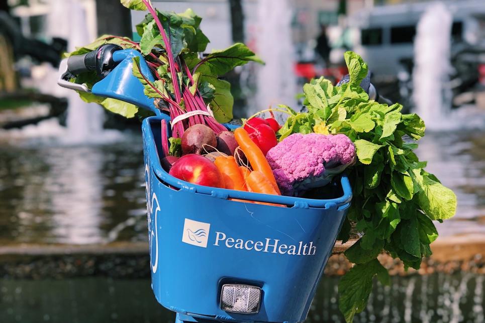 A blue PeaceHealth bicycle with a basket full of colorful vegetables.