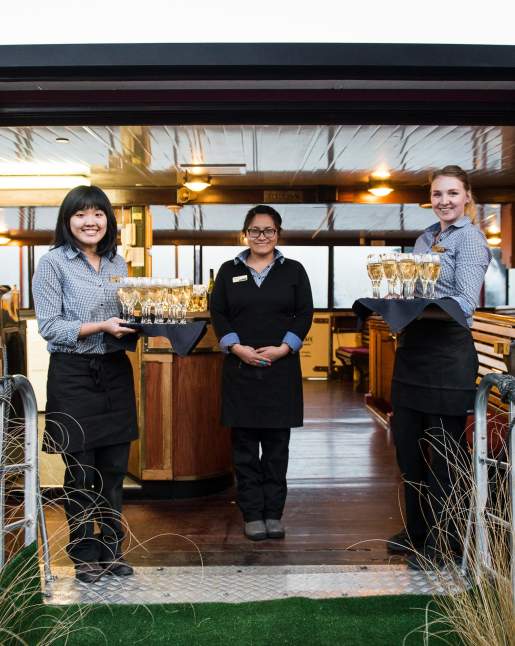 Waitresses waiting to greet guests onto a boat with trays of champagne