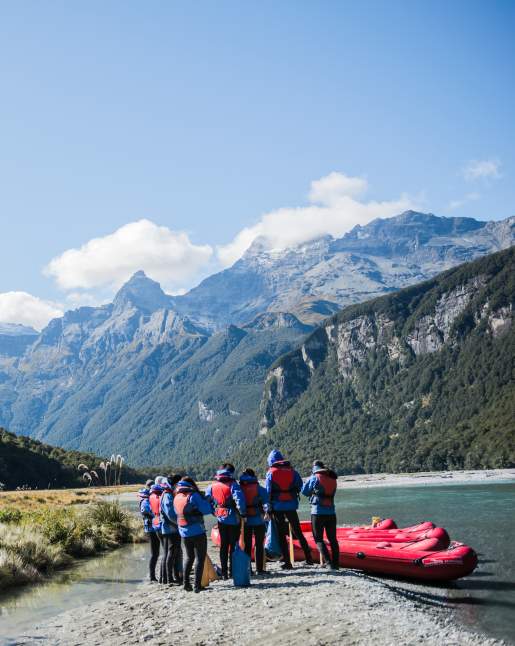 A group of people with inflatable kayaks standing by a river and surrounded by mountains