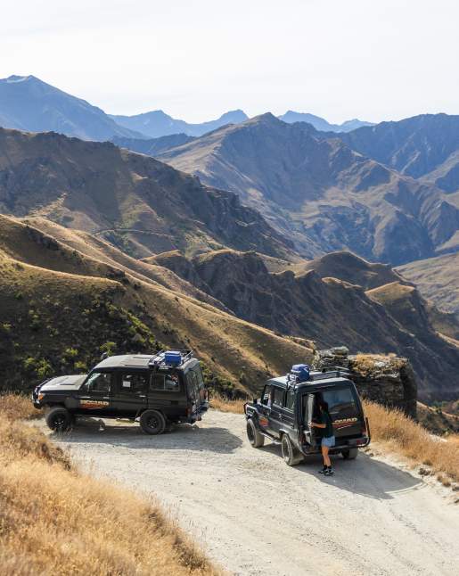 Two 4WD Landcruiser's parked up with a vast viewpoint of a big canyon and rugged mountains surrounding it.