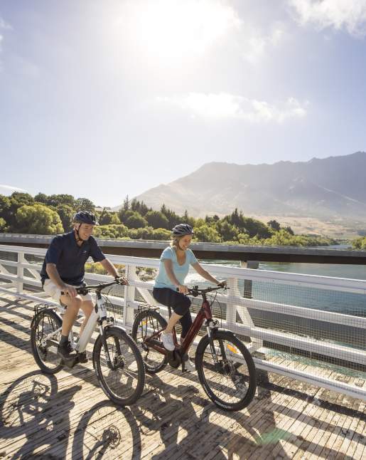 A couple biking the Queenstown Trail with the Remarkables Mountains in the background