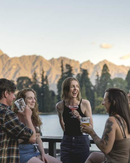 Friends laughing together with a drink in hand with lake and mountains in the background