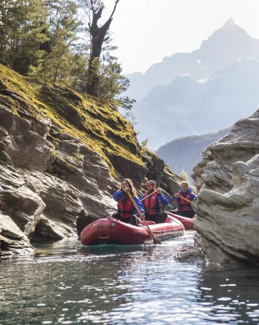 People on blow up kayaks paddling down a river surrounded by mountains