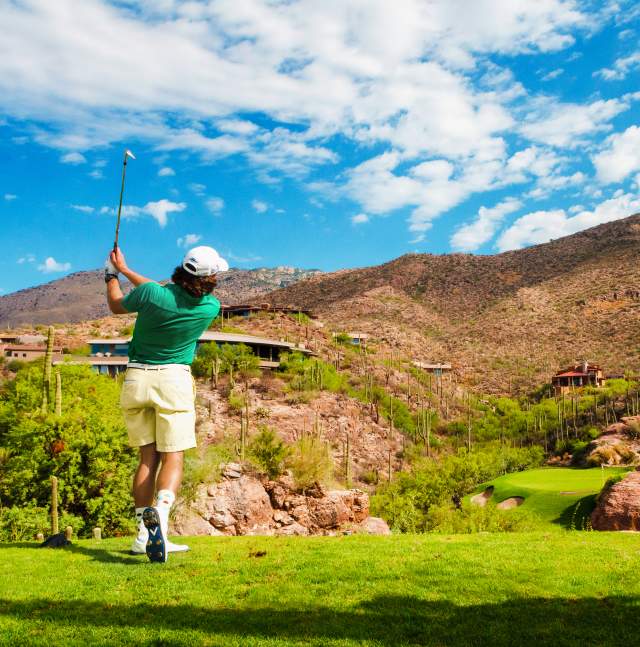 Back of man posed mid-golf-swing facing scenic desert mountains