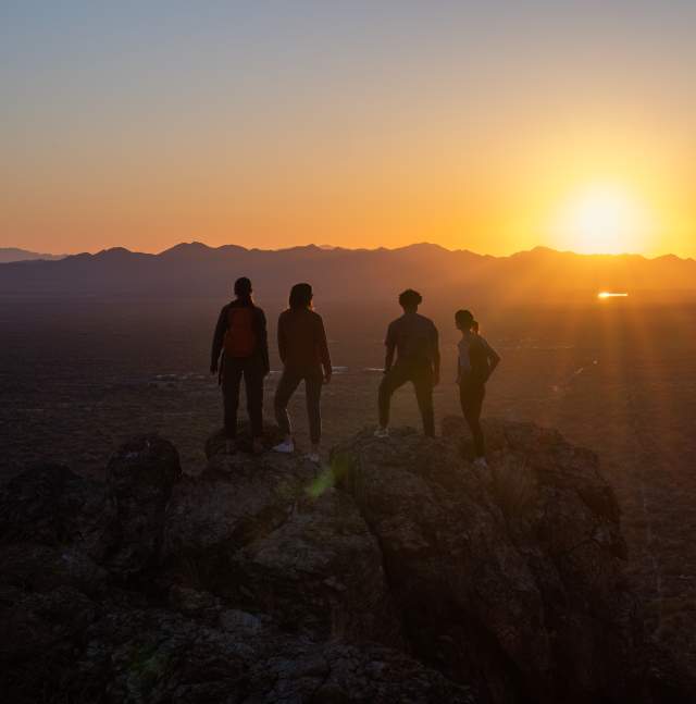 4 hikers stand at an overlook above Tucson looking into the sunset