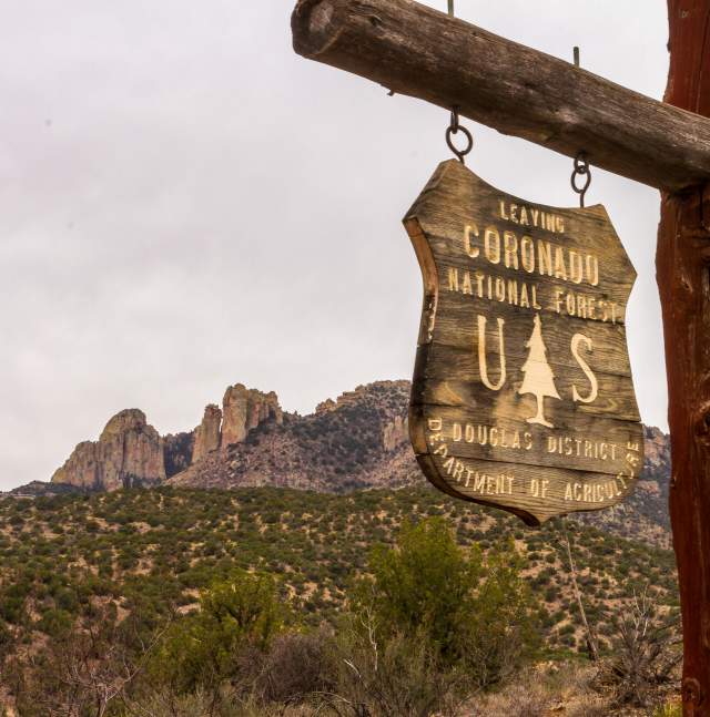 National forest sign that reads "Leaving Coronado National Park" with a desert landscape in  the background