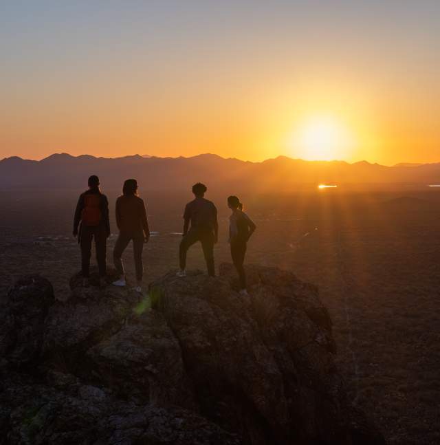 4 hikers stand at an overlook above Tucson looking into the sunset